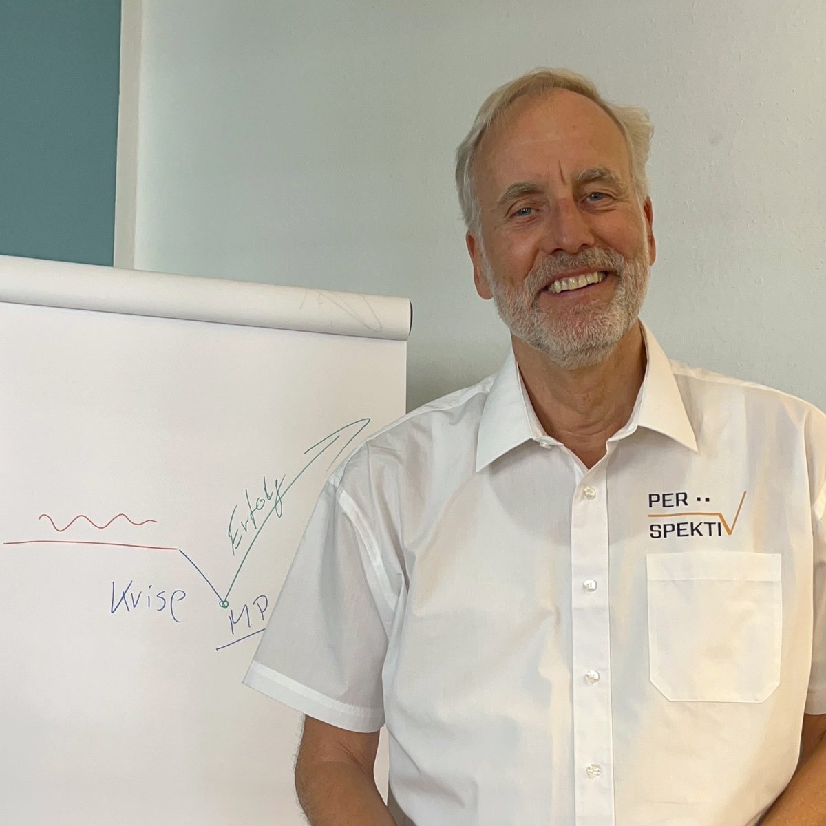 Ulrich Freund lächelt neben einem Flipchart mit einer Kurve von der Krise zum Erfolg